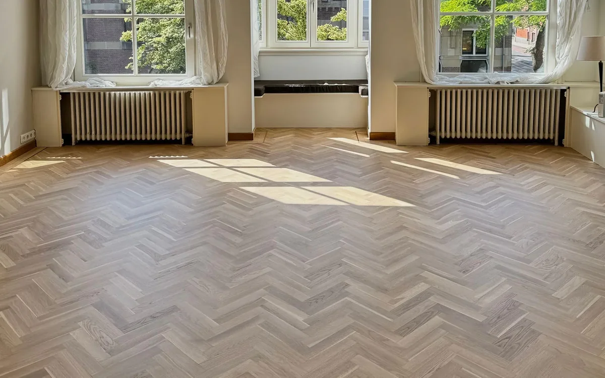 Net geschuurde visgraatvloer in een lichte, lege kamer, projectfoto van een vloerenbedrijf