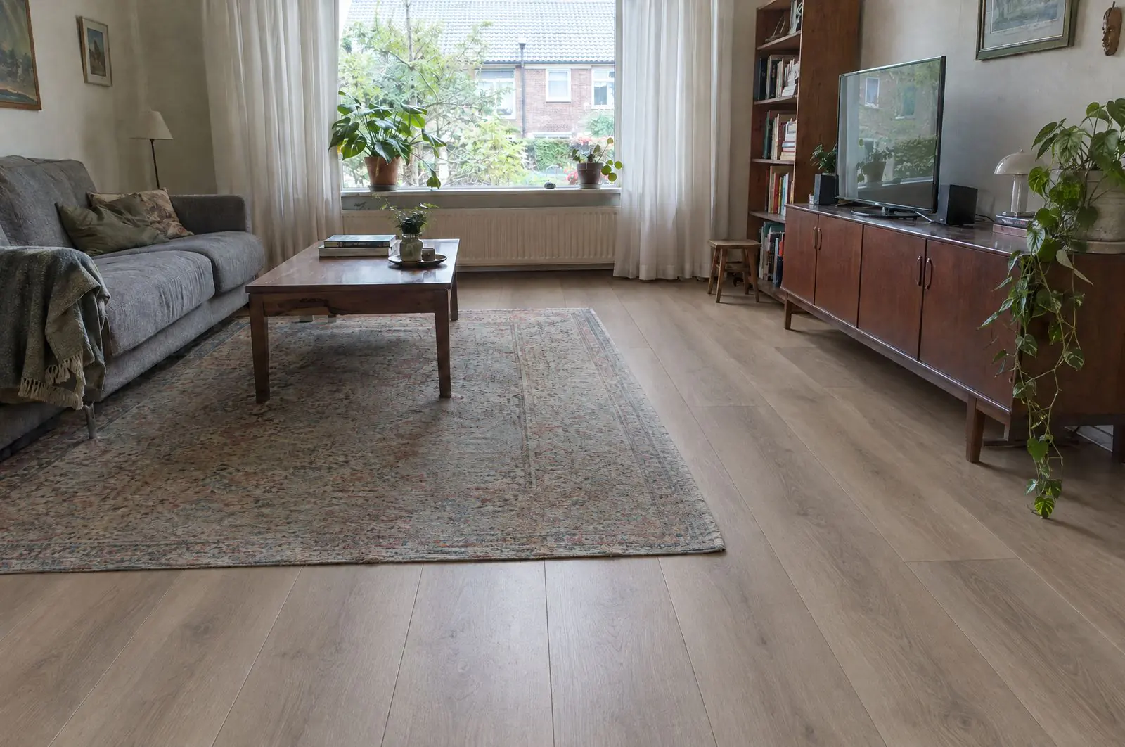 Na: dezelfde woonkamer met een grijs-beige PVC-vloer